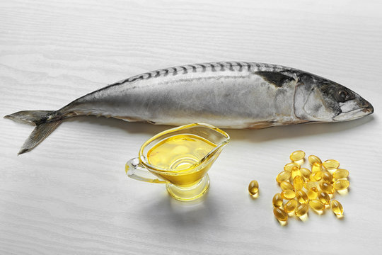 Fish oil pills and fresh fish on light background