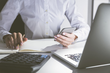 Close up of woman holding cell phone and taking notes