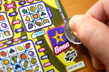 Close up man scratching lottery ticket on bonus section.