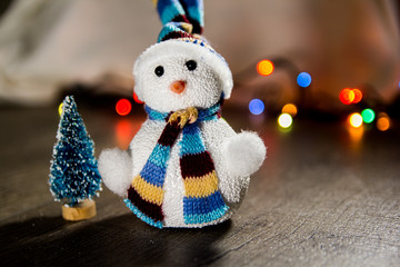 cute Christmas white snowman in a hat and a little Christmas toy tree in the background lights with place for text as substrate