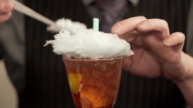 Young man working as a bartender in a nightclub bar. The bartender decorates cocktail with cotton candy. Cotton candy is dissolved in cocktail. Cotton candy
