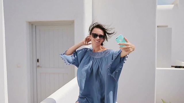 Beautiful woman with smart phone outdoors in old streets an Mykonos. Girl at street of typical greek traditional village with white walls and colorful doors on Mykonos Island, in Greece, Europe