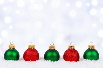 Red and green Christmas ornaments in snow with twinkling silver background