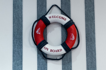 Safety first. Red lifebuoy with welcome aboard hanging on wall with blue white stripes