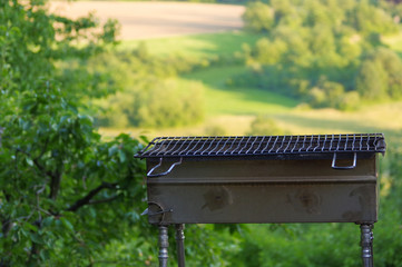 Empty portable BBQ grill in front of a fresh green summer landscape, close-up