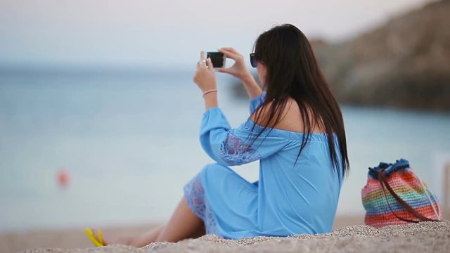 Young woman take a picture on phone on the beach at the evening
