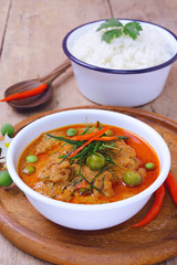 thai red curry fried with pork and coconut milk (panaeng) on white bowl with rice decorated by turkey berry and flower on wooden table.