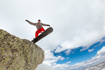 Snowboarder jumps from big rock