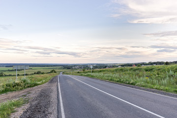 Vanishing straight highway through meadow at sunset in back lit. Silkovo, Kaluzhsky region, Russia.
