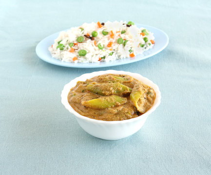 Indian food long green chili curry, a side dish, made from long, green pepper in a bowl and in the background is rice pilaf.