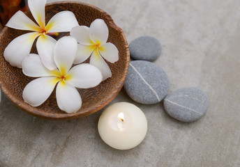 frangipani in wooden bowl with spa stones ,candle on grey background.

