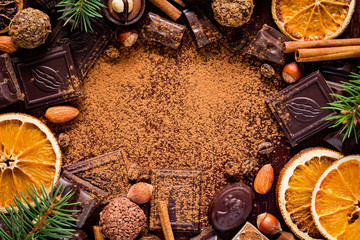 Christmas background with sweets: assortment of chocolates, truffles, candies, chocolate barks, spices and nuts with empty space for text. Horizontal
