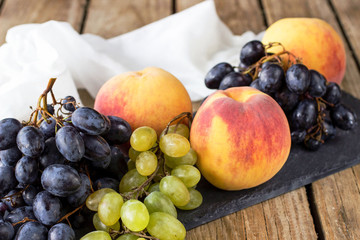 A bunch of grapes and ripe peaches on a black slate board on a wooden table