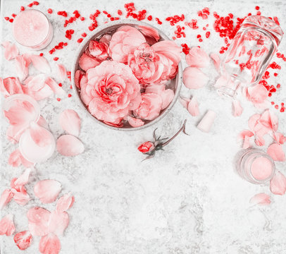 Wellness setting with roses, essential oil, bowl with water and flower petals on light background, top view, border