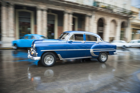Classic 1950s car drives in motion blur through the wet streets of Centro after a rainstorm in Havana, Cuba