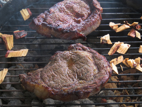Beef steaks on a hot charcoal grill with wood chips for smoking