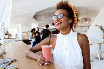 Young beautiful african girl drinking smoothie smiling resting in cafe.