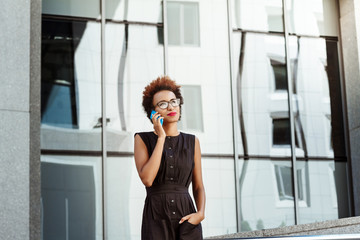 Beautiful african girl smiling speaking on phone walking down city.