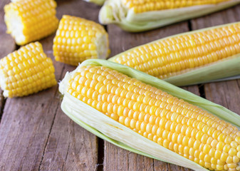 A whole fresh corn and pieces of corn on the wooden table