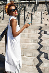 Young beautiful african girl smiling holding phone going up stairs.