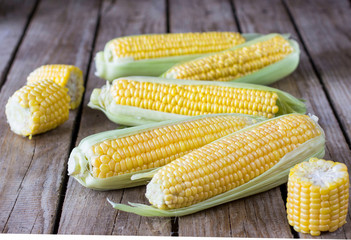 A whole fresh corn and pieces of corn on the wooden table