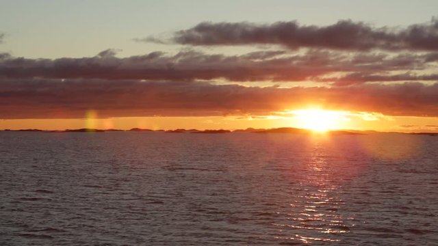 Sunset in the Atlantic Ocean. On the horizon the sun sets behind the rocks. The camera motion. Lofoten Islands, Norway.