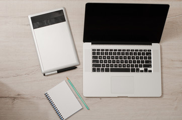 Top view of the open laptop, graphics tablet and notebook on a wooden table