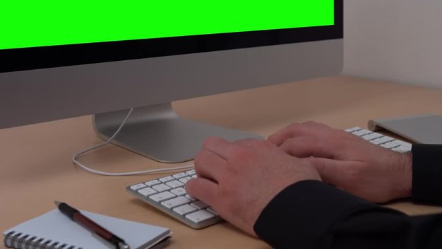 static shot of a man in his home office typing on a keyboard in front of a green screen computer display