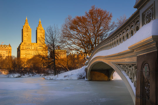 Cold Central Park winter sunrise on the frozen Lake with the Bow Bridge and Upper West Side buildings. Wintertime in Manhattan, New York City