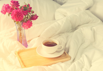 Cup of coffee and pink rose flower with wooden tray on bed backg