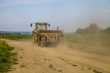 Fototapeta premium Tractor rides on the road near the potato field