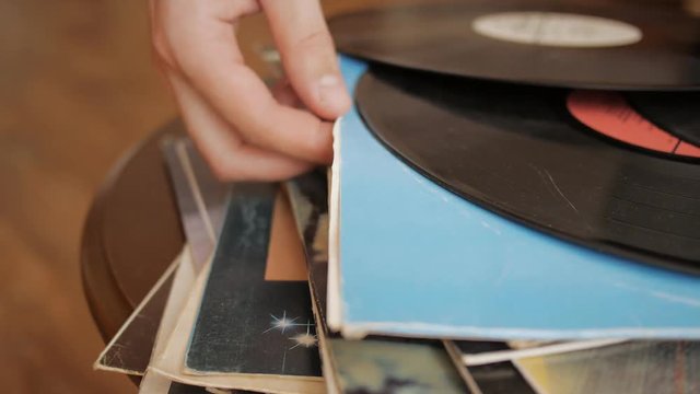 Close up of male hand gently pulls vintage vinyl record out of its cover in the LP collection stack.