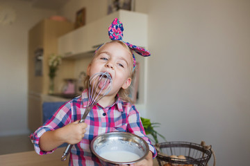 Funny little girl in checkered shirt whips up and licks a cream at home