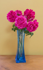 Pink rose bouquet in blue vase over yellow wall  on plank wooden