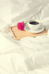 Cup of coffee and pink rose flower with wooden tray on bed backg