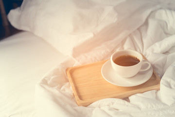 Fototapeta na wymiar Cup of coffee with wooden tray on bed background
