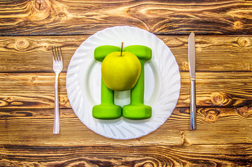 Dumbbells and apple on a plate as breakfast, concept of healthy lifestyle