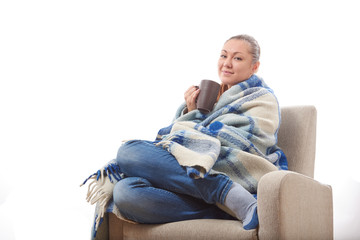 Beautiful girl resting and drinking tea sitting wrapped in a woolen plaid blanket.