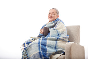 Beautiful girl resting and drinking tea sitting wrapped in a woolen plaid blanket.