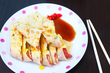 Close up of Taiwanese breakfast of egg pancake roll with bacon and corn on a plate.