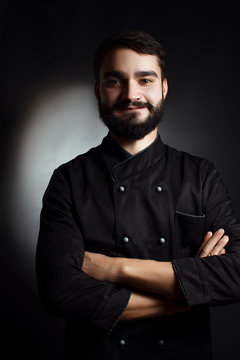 Professional chef with a beard in black uniform on a black background