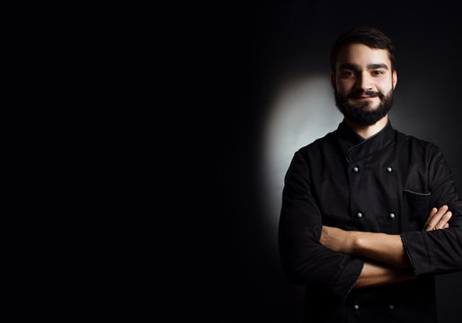 Professional chef with a beard in black uniform on a black background