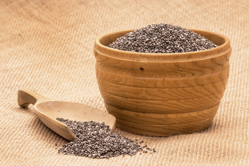 Wooden bowl full with chia seeds and a spoon next to it on sack cloth background seen from the side