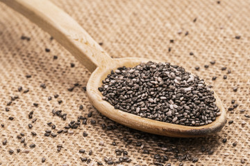 Wooden spoon full with chia seeds on sack cloth background