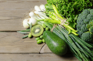 collection of fresh green vegetables ,broccoli,lettuce,avocado,kiwi,olives,green peppers and summer onions on rustic wooden table.Top view.Copy space..