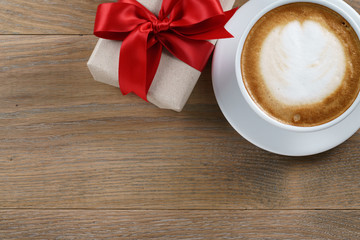 cup of cappuccino and gift on wooden oak table top view