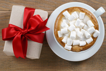 cup of cappuccino with marshmallow zand gift box on table