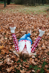 woman lying on autumn leaves, arms up in the sky