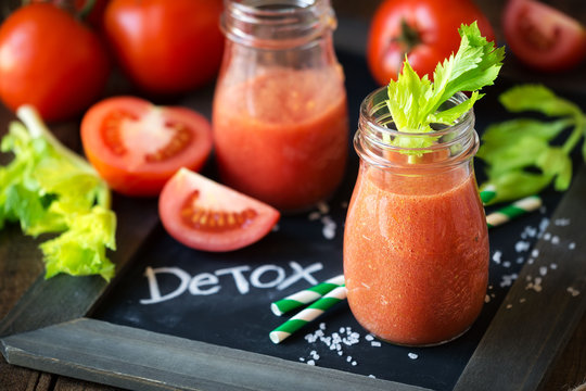 Fresh tomato and celery detox smoothie in a glass jar on a blask slate board with the word DETOX written on it