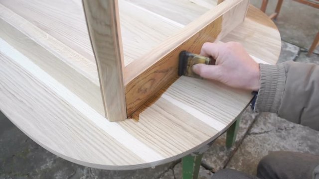 Carpenter is covering wooden table by lacquer. Worker making furniture and toning wood by paint